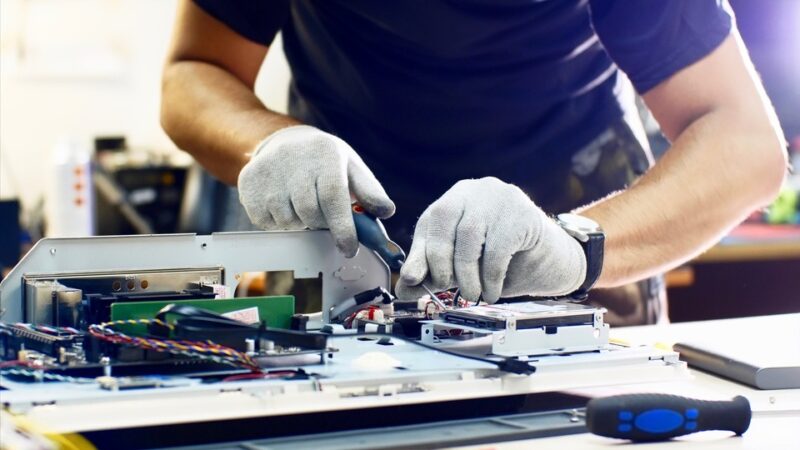 A person wearing gloves works on electronic components inside a computer, utilizing Parts as a Service to connect wires, bringing new value for old technology.