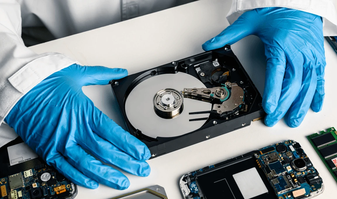 Person in gloves examining a hard drive among electronic components on a table