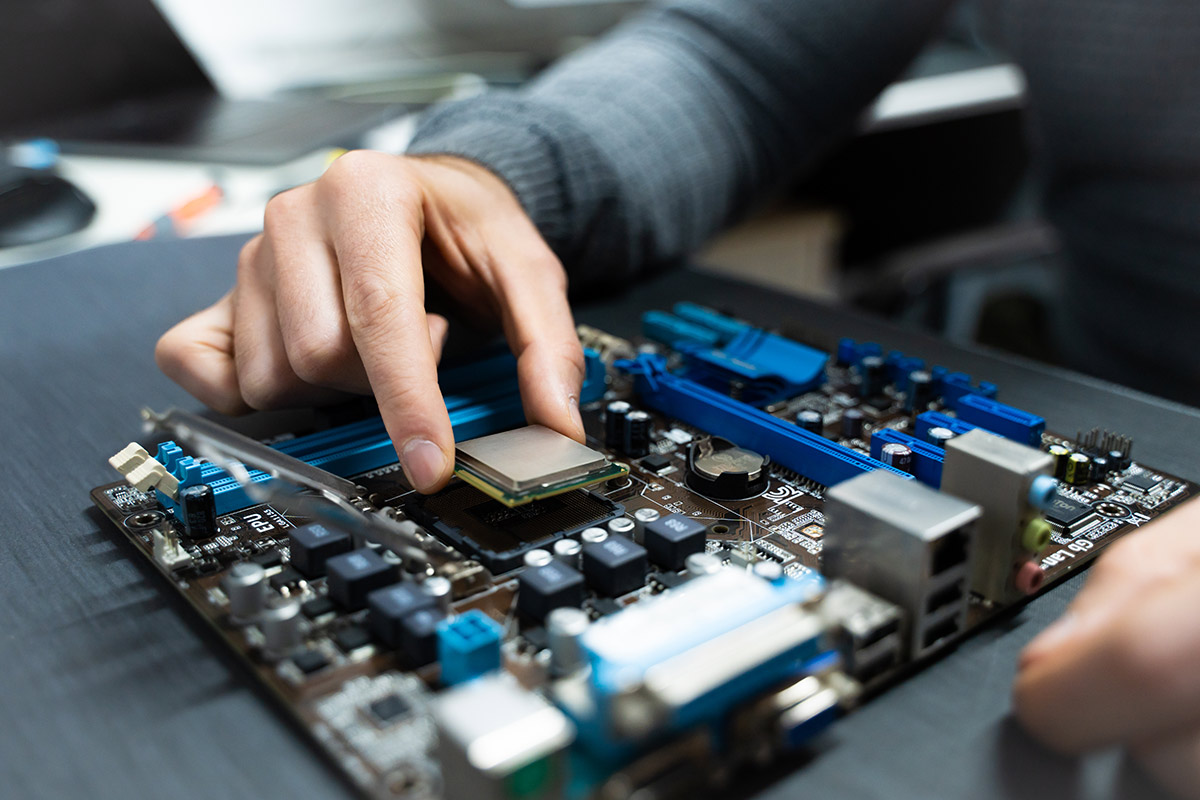 A person installs a CPU onto a computer motherboard, surrounded by various components on a table.