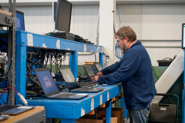 Technician troubleshooting multiple laptops on a workbench in a tech workshop