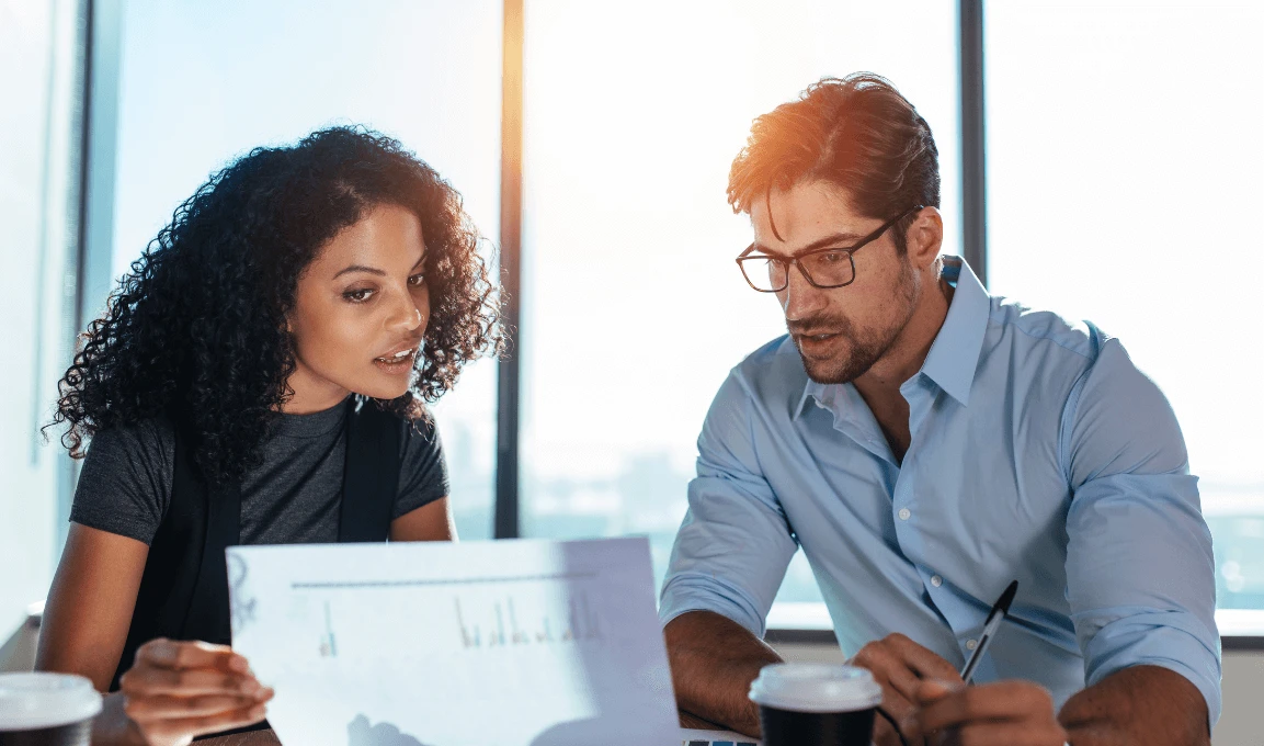 Two colleagues reviewing a document with charts in a sunlit office setting