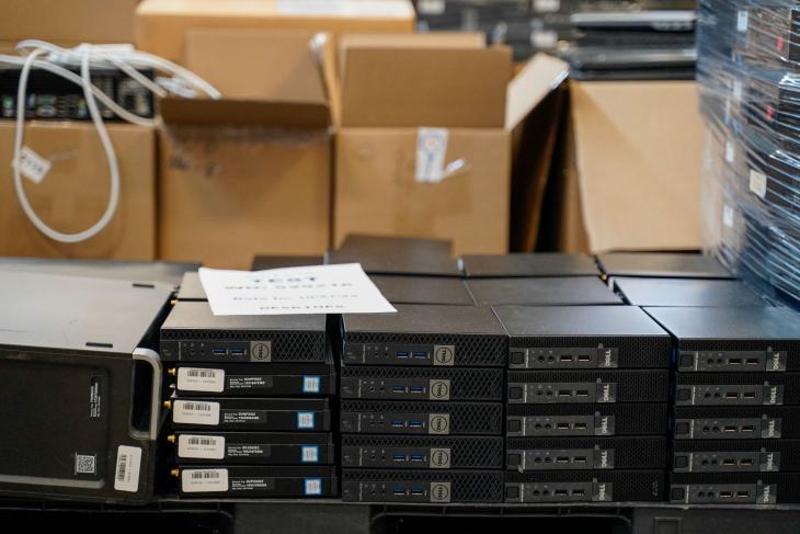 Stacked black computer towers sit in front of open cardboard boxes, ready for secure data destruction. A white paper is placed on top of the computers, ensuring business compliance and safeguarding sensitive information.